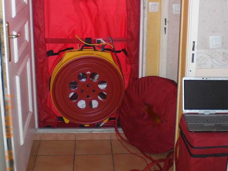 Porte soufflante rouge installée dans l'encadrement d'une porte d'entrée, prête pour la mesure